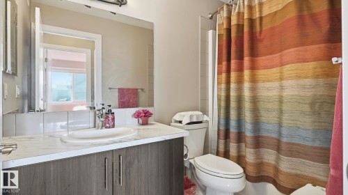 Bathroom featuring a vanity with a white countertop and an undermount sink, a large wall-mounted mirror, a toilet, and a shower/tub combination with tiled walls - 731 36 Street Sw, Edmonton, AB - Indoor Photo Showing Bathroom