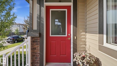 Red entry door with an integrated glass panel, complemented by sidelight windows, tan horizontal siding, dark brick, and white porch railings - 731 36 Street Sw, Edmonton, AB - Outdoor With Exterior
