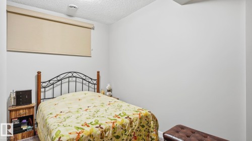 Bedroom featuring light-colored walls, textured ceiling, a window with a roller shade, and wood-finish flooring - 731 36 Street Sw, Edmonton, AB - Indoor Photo Showing Bedroom