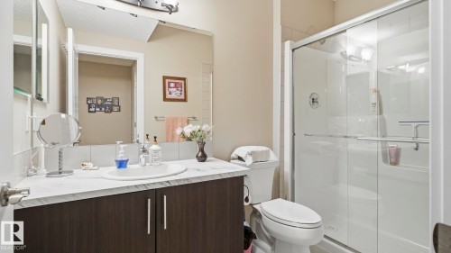 Bathroom featuring a dark wood-finish vanity with a white countertop and integrated sink, a large wall-mounted mirror, a glass-enclosed shower, and neutral wall tones - 731 36 Street Sw, Edmonton, AB - Indoor Photo Showing Bathroom