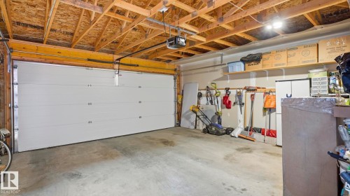 Spacious garage featuring a large overhead door, concrete flooring, exposed ceiling joists, wall-mounted shelving, and overhead lighting - 731 36 Street Sw, Edmonton, AB - Indoor Photo Showing Garage