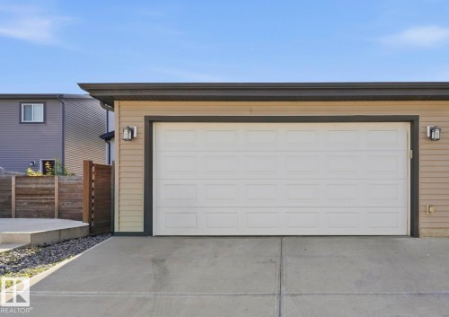 Single-car garage with a paneled white door, bordered by dark trim and tan siding - 731 36 Street Sw, Edmonton, AB - Outdoor With Exterior