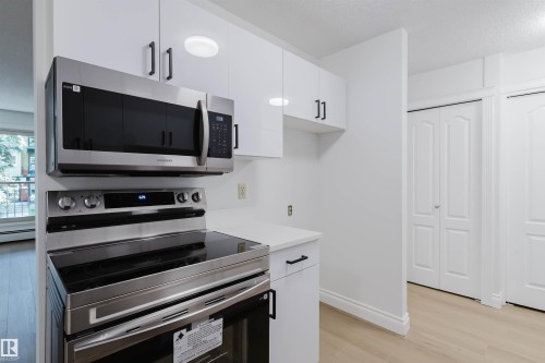 Stainless steel microwave and range, white cabinetry with black hardware, white countertops, and light wood-finish flooring - #106 10520 80 Av Nw, Edmonton, AB - Indoor Photo Showing Kitchen