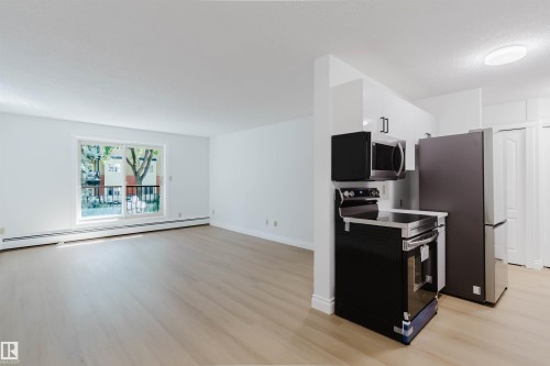 Wood-finish flooring, white walls, and a sliding glass door to a balcony - #106 10520 80 Av Nw, Edmonton, AB - Indoor Photo Showing Kitchen