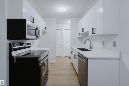 Modern kitchen featuring white cabinetry, stainless steel appliances, light-toned wood-finish flooring, and white countertops - #106 10520 80 Av Nw, Edmonton, AB - Indoor Photo Showing Kitchen With Double Sink With Upgraded Kitchen