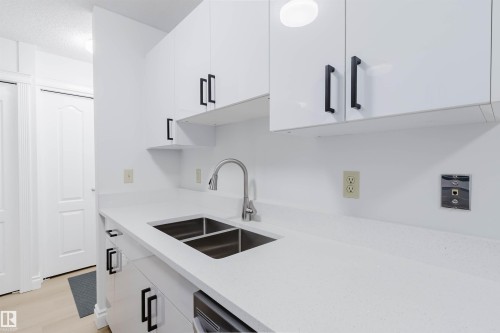 White cabinetry with matte black pulls, stainless steel double basin sink, chrome faucet, and light-toned countertop - #106 10520 80 Av Nw, Edmonton, AB - Indoor Photo Showing Kitchen With Double Sink