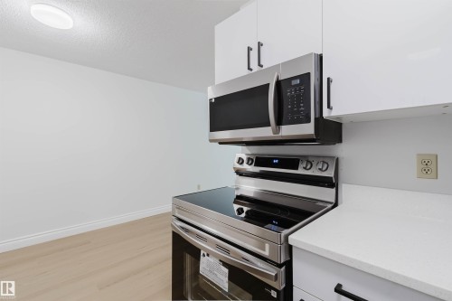 Stainless steel oven with a glass cooktop, stainless steel microwave, white cabinetry with black hardware, and white countertops - #106 10520 80 Av Nw, Edmonton, AB - Indoor Photo Showing Kitchen