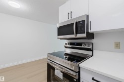 Stainless steel oven with a glass cooktop, stainless steel microwave, white cabinetry with black hardware, and white countertops - 