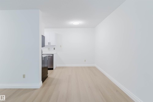 Recessed kitchen area with white cabinetry, stainless steel dishwasher, and refrigerator - #106 10520 80 Av Nw, Edmonton, AB - Indoor Photo Showing Other Room