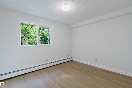 Light wood-finish flooring, white walls, and a large window providing natural illumination - #106 10520 80 Av Nw, Edmonton, AB - Indoor Photo Showing Other Room