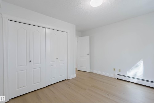 Light wood-finish flooring, white walls, white bi-fold closet doors, white baseboards, and a flush-mount ceiling light - #106 10520 80 Av Nw, Edmonton, AB - Indoor Photo Showing Other Room
