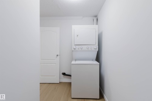 Dedicated laundry area featuring a white stacked washer and dryer unit, wood-finish flooring, and a white paneled door - #106 10520 80 Av Nw, Edmonton, AB - Indoor Photo Showing Laundry Room