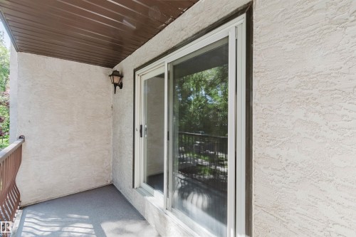 Balcony with textured exterior, a white frame sliding glass door, overhead lighting, a brown slatted ceiling, and an ornate brown metal railing - #106 10520 80 Av Nw, Edmonton, AB - Outdoor With Exterior