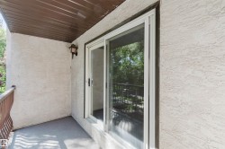 Balcony with textured exterior, a white frame sliding glass door, overhead lighting, a brown slatted ceiling, and an ornate brown metal railing - 