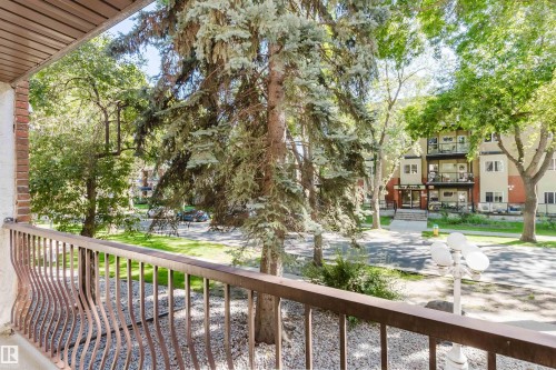 Balcony with decorative metal railing and brick accent, overlooking mature trees and landscaped grounds - #106 10520 80 Av Nw, Edmonton, AB - Outdoor With Balcony