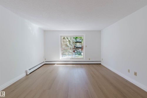 Light wood-finish flooring, white walls, and a sliding glass door to a balcony - #106 10520 80 Av Nw, Edmonton, AB - Indoor Photo Showing Other Room