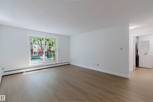 Expansive room with wood-finish flooring, white walls, and a sliding glass door - #106 10520 80 Av Nw, Edmonton, AB - Indoor