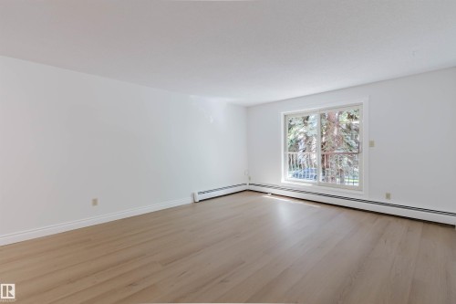 Expansive room featuring wood-finish flooring, white walls, and a sliding glass door providing outdoor access - #106 10520 80 Av Nw, Edmonton, AB - Indoor Photo Showing Other Room