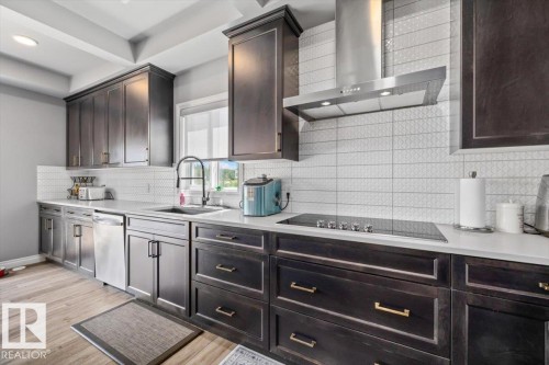 Dark wood-finish cabinetry with gold-tone hardware, white countertops, stainless steel appliances, and a pattern tile backsplash - 5203 23A Avenue Sw, Edmonton, AB - Indoor Photo Showing Kitchen With Upgraded Kitchen