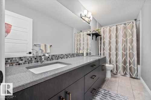 Dual integrated sinks, grey countertop, mosaic tile backsplash, dark wood-finish vanity, and bronze-finish hardware - 5203 23A Avenue Sw, Edmonton, AB - Indoor Photo Showing Bathroom