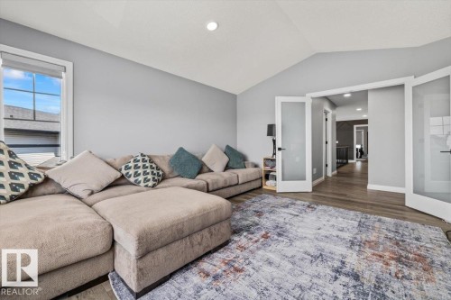 Vaulted ceiling, recessed lighting, wood-finish flooring, white trim, and frosted glass French doors - 5203 23A Avenue Sw, Edmonton, AB - Indoor Photo Showing Living Room