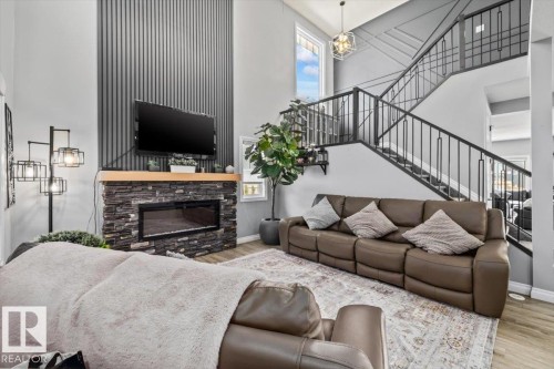 Two-story living area with a stone-clad fireplace, wood-finish mantel, and a prominent staircase featuring a wrought-iron railing - 5203 23A Avenue Sw, Edmonton, AB - Indoor Photo Showing Living Room With Fireplace
