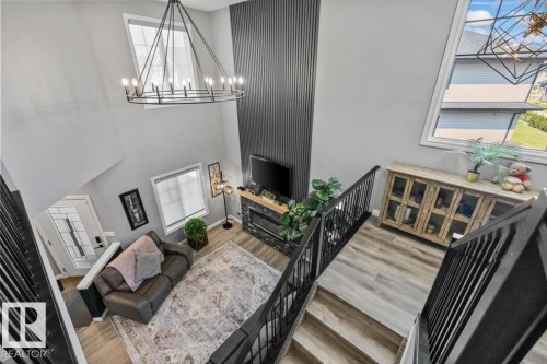 Two-story foyer with a large chandelier, wood-finish flooring, and black metal railings - 5203 23A Avenue Sw, Edmonton, AB - Indoor Photo Showing Other Room