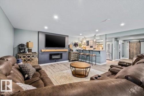 Open-concept living area with wood-finish flooring, a built-in electric fireplace, recessed lighting, a breakfast bar with pendant lighting, and a barn door - 5203 23A Avenue Sw, Edmonton, AB - Indoor Photo Showing Living Room With Fireplace