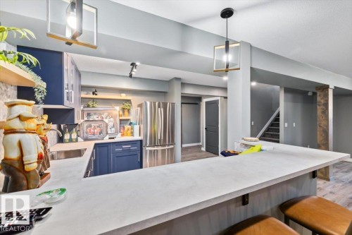 Kitchenette featuring blue cabinetry, stainless steel appliances, open shelving, and a stone-look countertop with bar seating - 5203 23A Avenue Sw, Edmonton, AB - Indoor