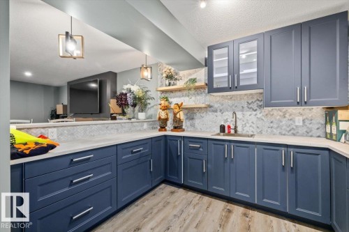 Modern cabinetry with integrated sink, wood-finish flooring, light-toned countertops, and mosaic tile backsplash - 5203 23A Avenue Sw, Edmonton, AB - Indoor Photo Showing Kitchen