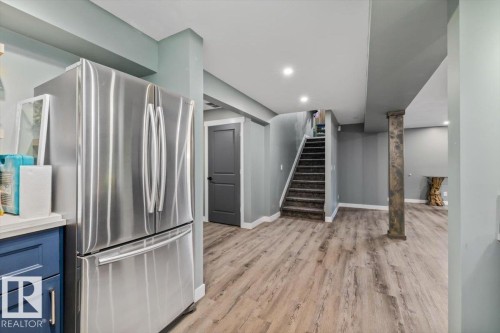 Stainless steel refrigerator, wood-finish flooring, recessed lighting, carpeted stairs, and a dark paneled door - 5203 23A Avenue Sw, Edmonton, AB - Indoor Photo Showing Other Room