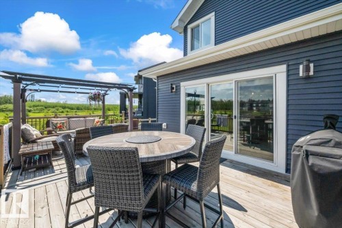 Expansive composite deck featuring a round dining table with seating for multiple guests, pergola with overhead lattice structure, and wide glass sliding doors opening directly from the primary residence - 5203 23A Avenue Sw, Edmonton, AB - Outdoor With Deck Patio Veranda With Exterior