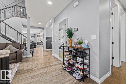 Wood-finish flooring, white trim, and a black wrought iron staircase create a contemporary entry - 5203 23A Avenue Sw, Edmonton, AB - Indoor