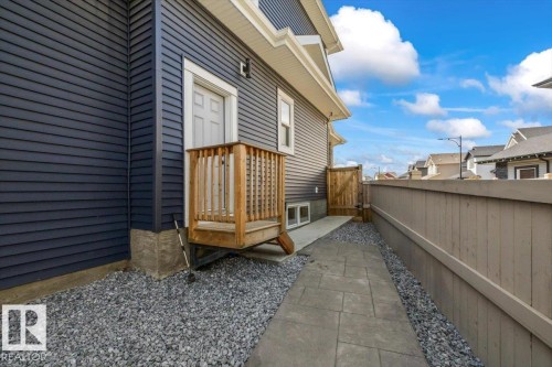 Dark blue horizontal siding with white trim, wooden deck with railing, concrete foundation, gravel landscaping, paved walkway, and wooden fence - 5203 23A Avenue Sw, Edmonton, AB - Outdoor