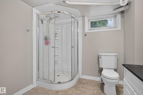Compact corner shower enclosure with a curved glass door, white acrylic base, and integrated shelving - 11549 88 Street Nw, Edmonton, AB - Indoor Photo Showing Bathroom