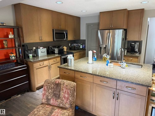 Kitchen featuring wood-finish cabinetry, stainless steel appliances, granite countertops, an island with an undermount sink, and recessed lighting - 7065 Cardinal Way Sw, Edmonton, AB - Indoor Photo Showing Kitchen