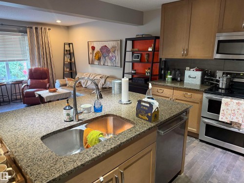 Kitchen island with an undermount sink, granite-style countertop, and stainless steel dishwasher - 7065 Cardinal Way Sw, Edmonton, AB - Indoor Photo Showing Kitchen
