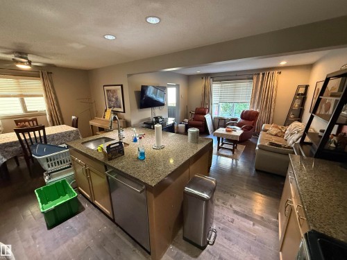 Kitchen island with integrated sink, stainless steel dishwasher, and stone-finish countertop - 7065 Cardinal Way Sw, Edmonton, AB - Indoor