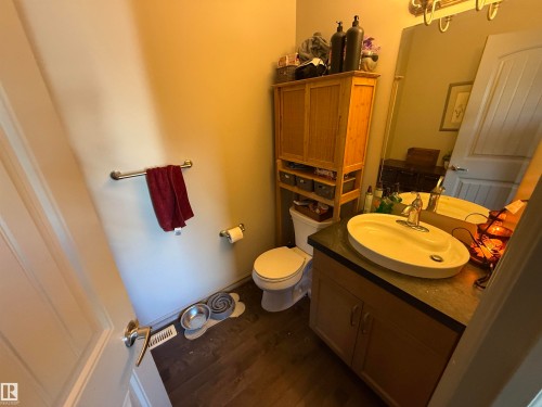 Wood-finish flooring, single vanity with oval basin, and a wall-mounted mirror - 7065 Cardinal Way Sw, Edmonton, AB - Indoor Photo Showing Bathroom