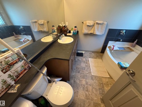 Dual vanity with integrated sinks, dark countertop, and tiled flooring - 7065 Cardinal Way Sw, Edmonton, AB - Indoor Photo Showing Bathroom