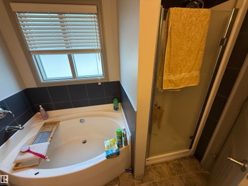 Soaking tub with dark tile surround and window, accompanied by a glass-enclosed shower - 7065 Cardinal Way Sw, Edmonton, AB - Indoor Photo Showing Bathroom