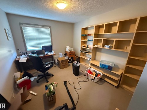 Built-in shelving unit with varied compartment sizes, flush-mounted ceiling light fixture, and a window with horizontal blinds - 7065 Cardinal Way Sw, Edmonton, AB - Indoor Photo Showing Office