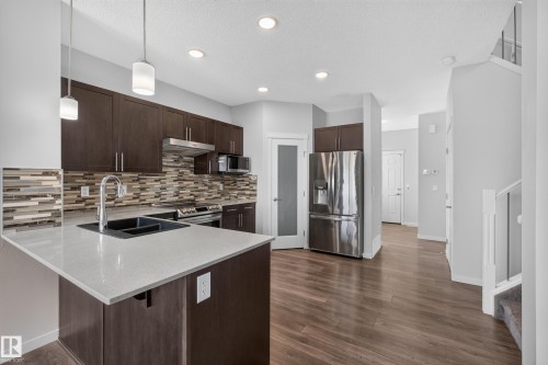 Kitchen featuring dark wood-finish cabinetry, light-toned countertops, and a full tile backsplash - 1404 25 Avenue Nw, Edmonton, AB - Indoor Photo Showing Kitchen With Double Sink With Upgraded Kitchen