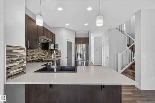 Kitchen featuring an island with a double basin sink, dark wood-finish cabinetry, stainless steel appliances, and a mosaic tile backsplash - 1404 25 Avenue Nw, Edmonton, AB - Indoor Photo Showing Kitchen With Double Sink With Upgraded Kitchen