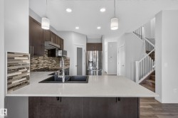 Kitchen featuring an island with a double basin sink, dark wood-finish cabinetry, stainless steel appliances, and a mosaic tile backsplash - 