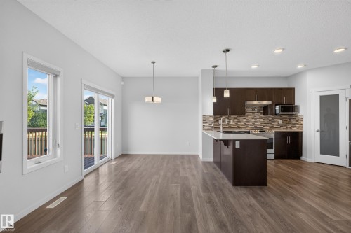 Modern kitchen with wood-finish flooring, dark wood cabinetry, a center island with pendant lighting, and a patterned tile backsplash - 1404 25 Avenue Nw, Edmonton, AB - Indoor Photo Showing Kitchen With Upgraded Kitchen