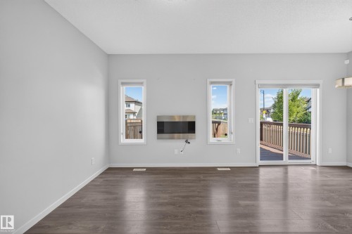 Wood-finish flooring throughout, bright white walls, two vertical windows, a built-in electric fireplace, and a glass sliding door leading to an exterior deck - 1404 25 Avenue Nw, Edmonton, AB - Indoor