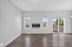 Wood-finish flooring throughout, bright white walls, two vertical windows, a built-in electric fireplace, and a glass sliding door leading to an exterior deck - 