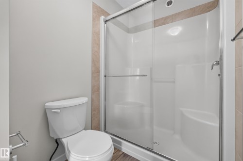 White toilet with a built-in shower featuring a sliding glass door and an integrated bench - 1404 25 Avenue Nw, Edmonton, AB - Indoor Photo Showing Bathroom