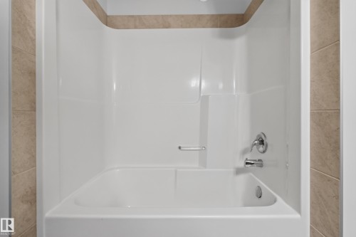 White bathtub and shower surround with integrated soap dish, featuring chrome fixtures and tile detailing - 1404 25 Avenue Nw, Edmonton, AB - Indoor Photo Showing Bathroom